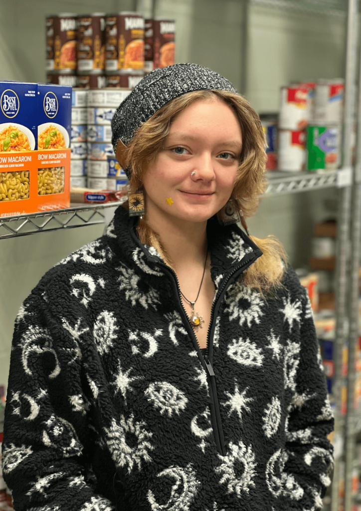A women in a black and white jacket standing in front of food shelves.