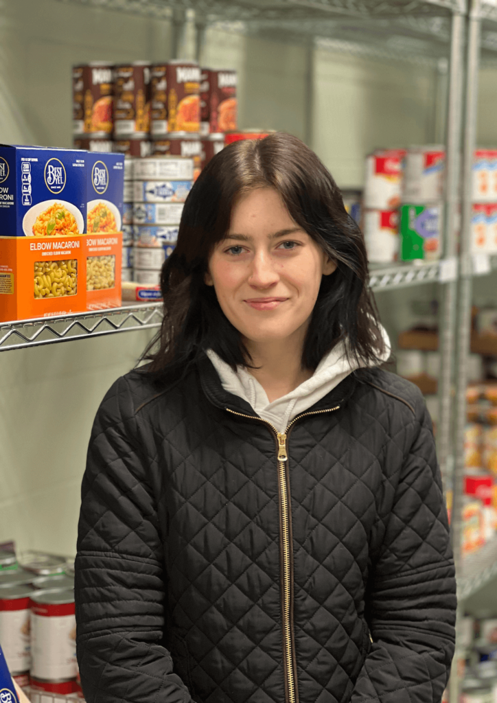 A woman with brown hair standing in front of food shelves.