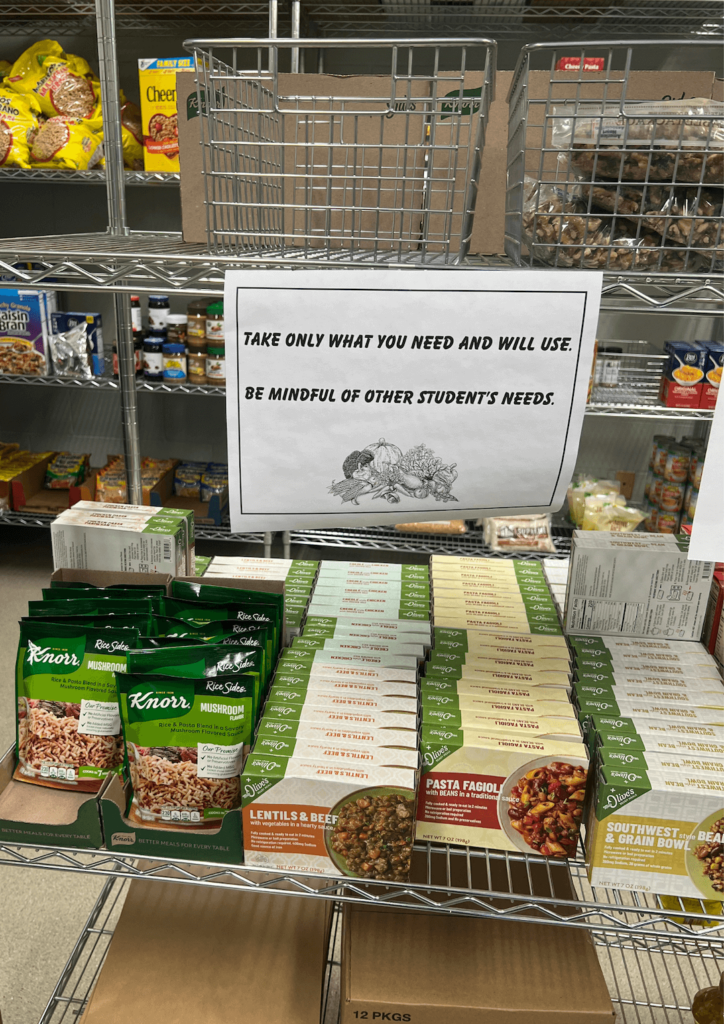 Shelves of food with a sign that says "Take only what you need and will use. Be mindful of other student's needs". 