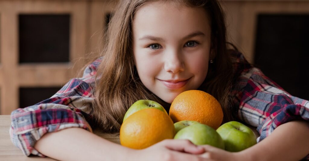 A young girl holding various fruits and smiling